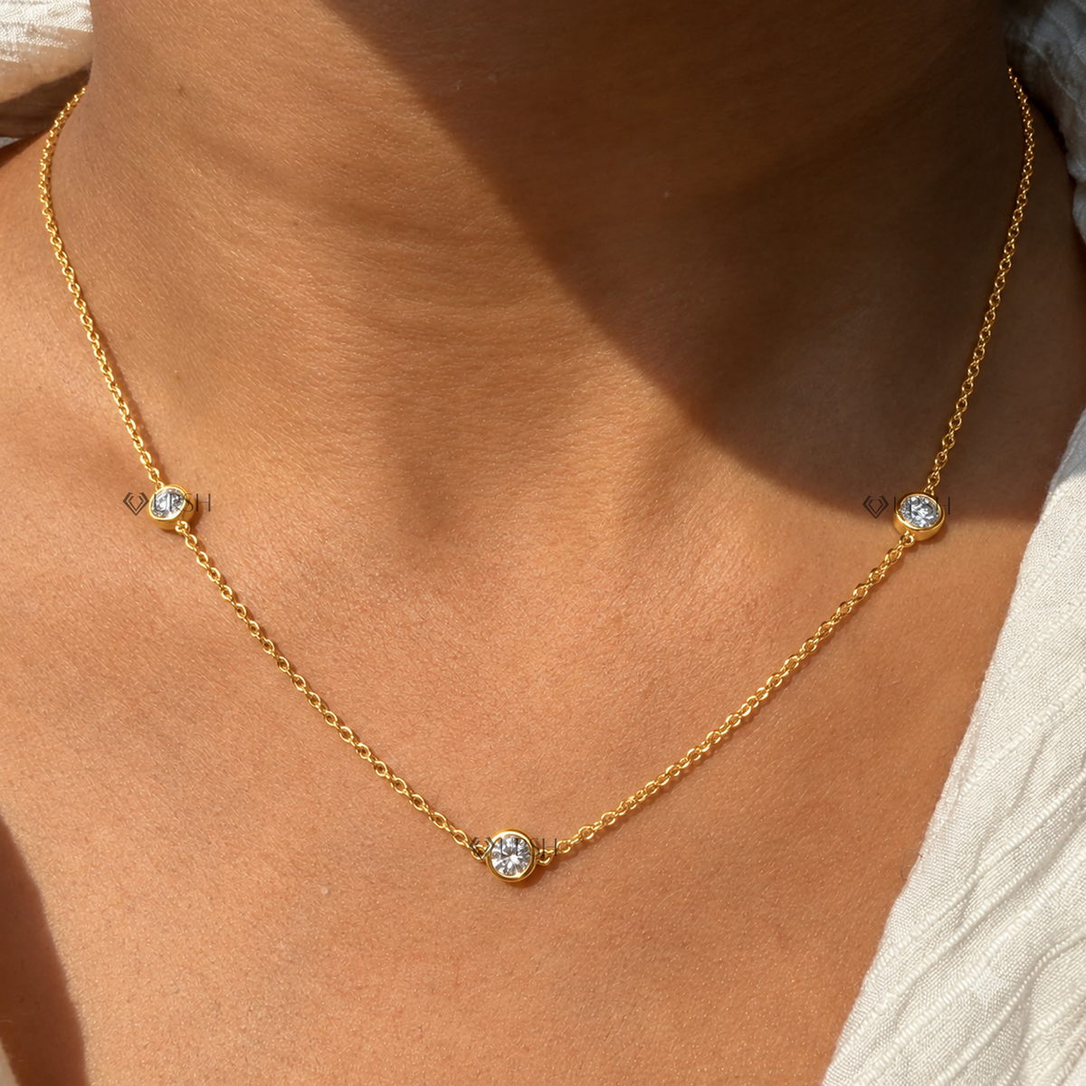 Yellow gold three stone bezel set diamond station necklace styled gracefully on neck in natural daylight