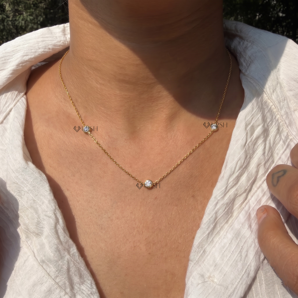 Daylight perspective of yellow gold three stone bezel set floating diamond chain worn against collarbone
