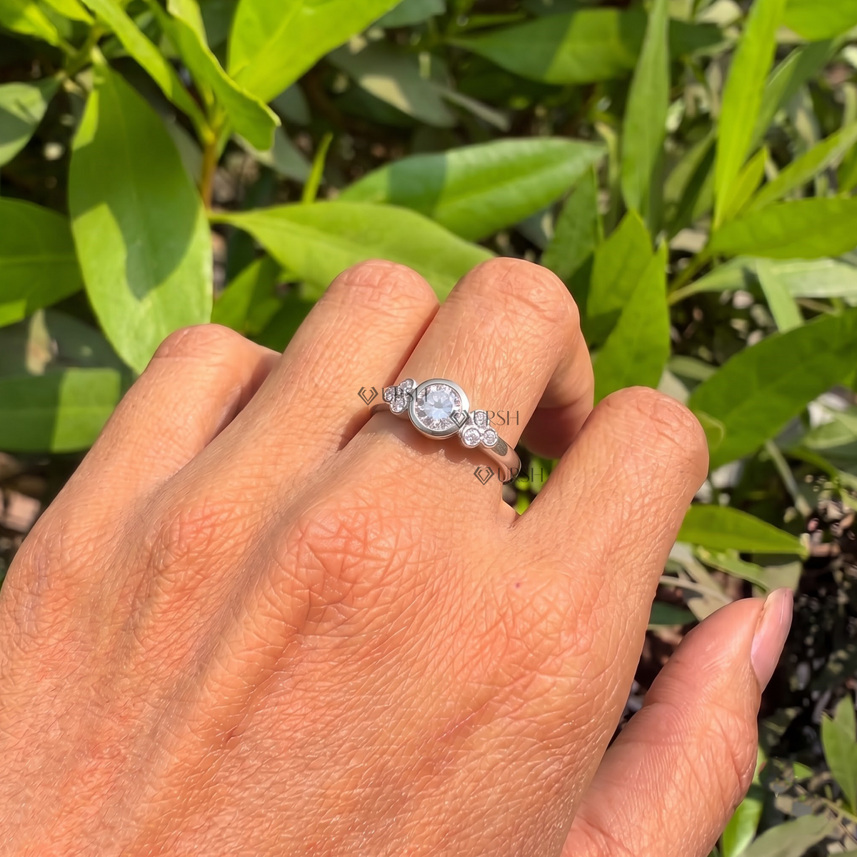 White gold bezel cluster diamond ring worn against natural garden greenery