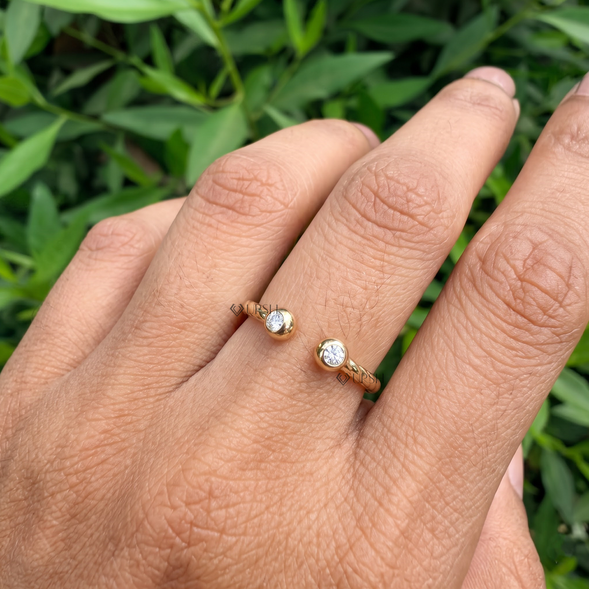 Wide daylight perspective of twisted open bypass ring worn against garden foliage
