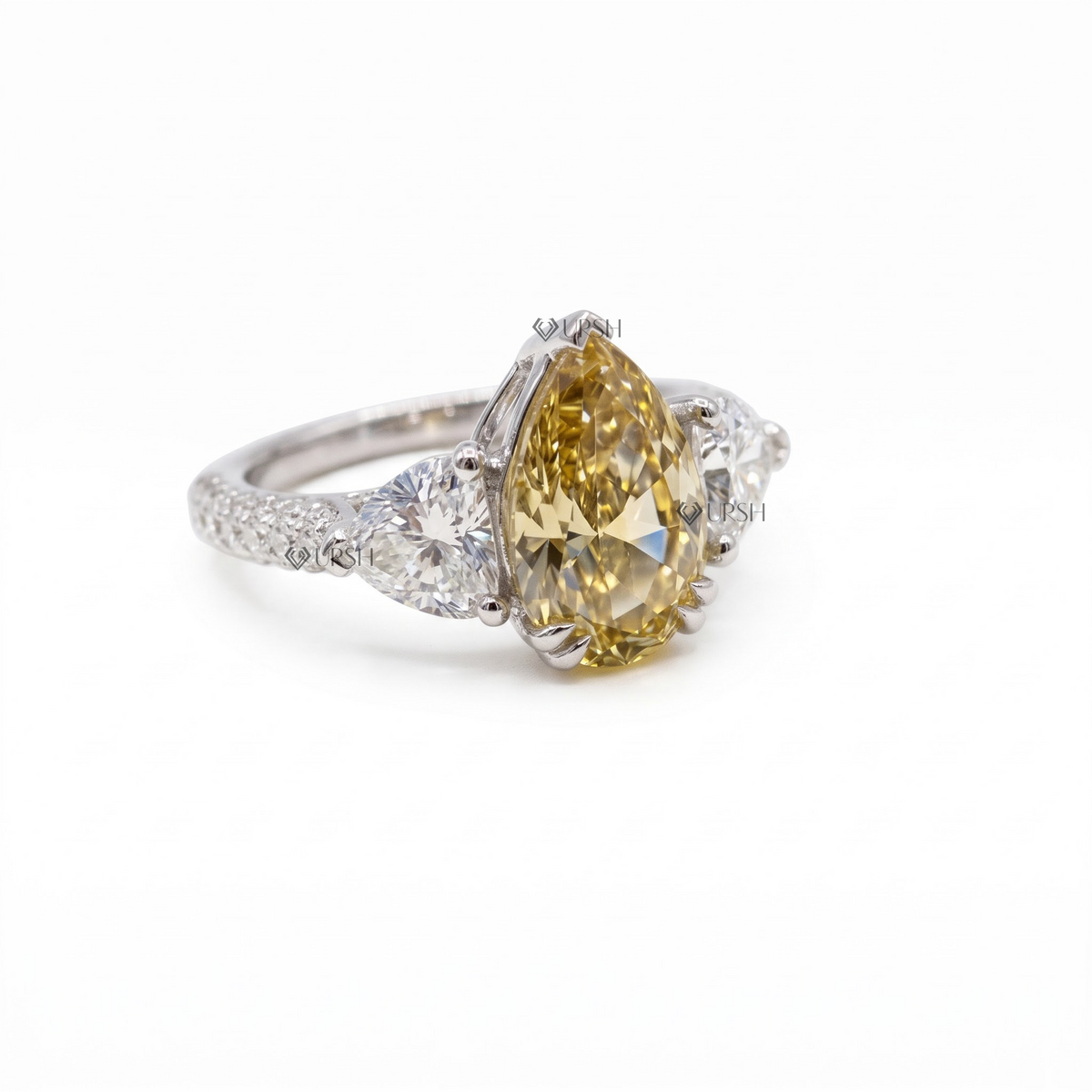 Solid white gold three-stone pear diamond ring with sparkling micro-pavé shank on clean white background