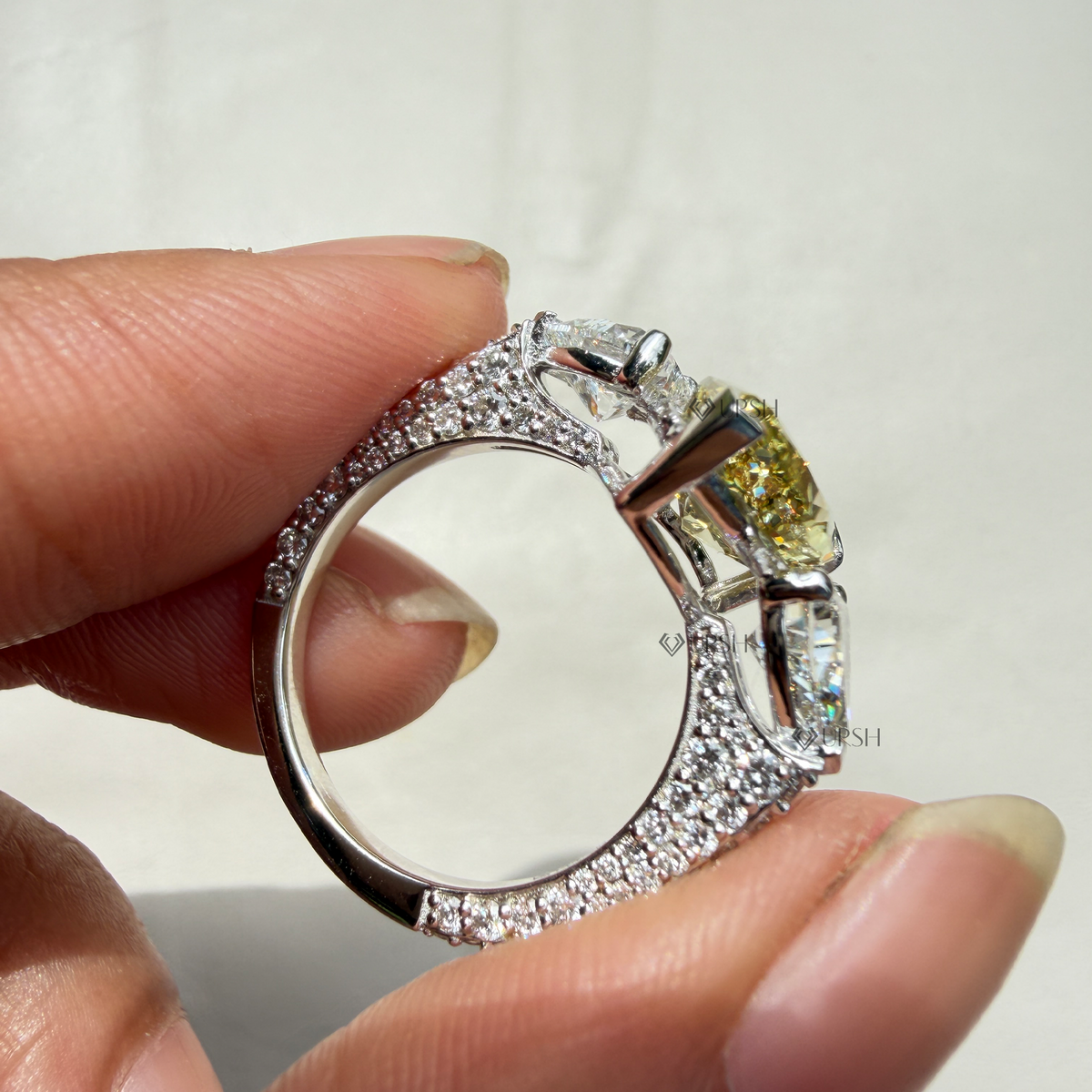 Detailed macro view holding solid gold yellow pear trilogy ring displaying full pavé band interior and V-prongs