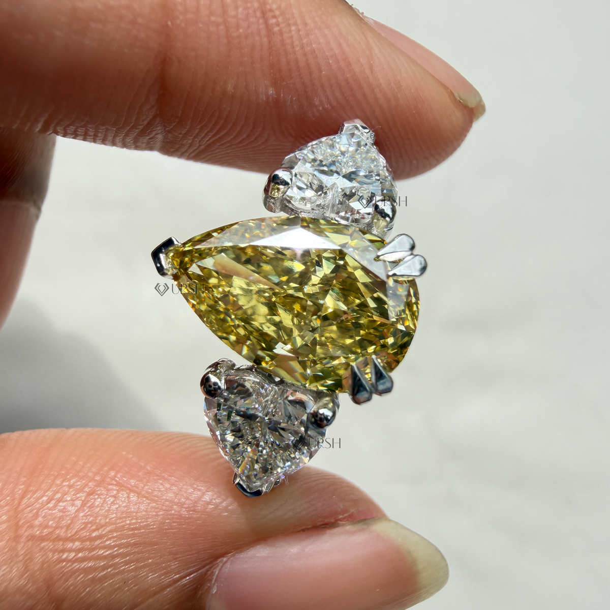 Holding two-tone yellow pear diamond ring showcasing side pear stone brilliance and shoulder pavé