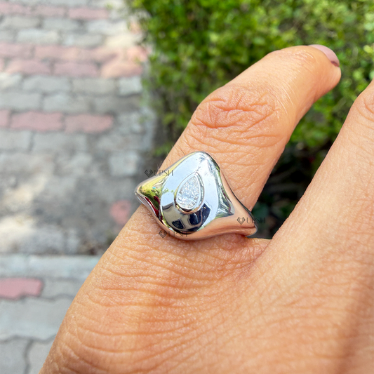 Sculpted white gold pear diamond signet ring worn on index finger in natural daylight