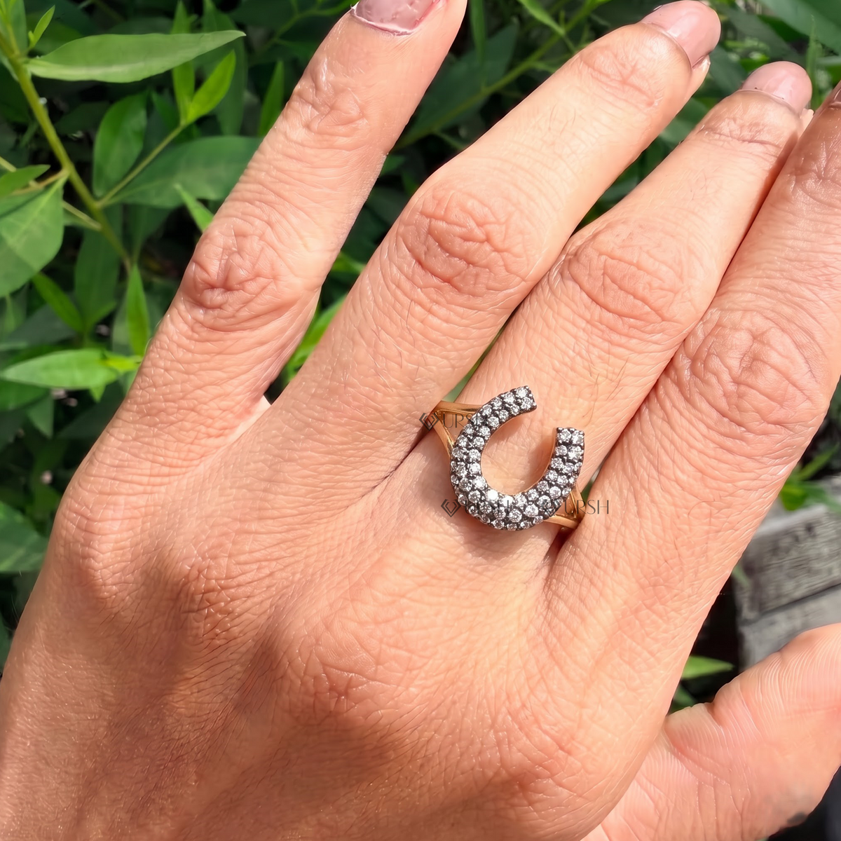 Chunky diamond horseshoe cocktail ring styled on hand against garden greenery