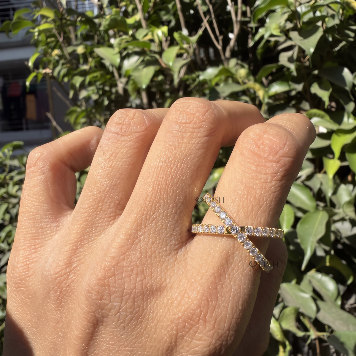 Yellow gold criss-cross diamond ring worn against natural garden greenery