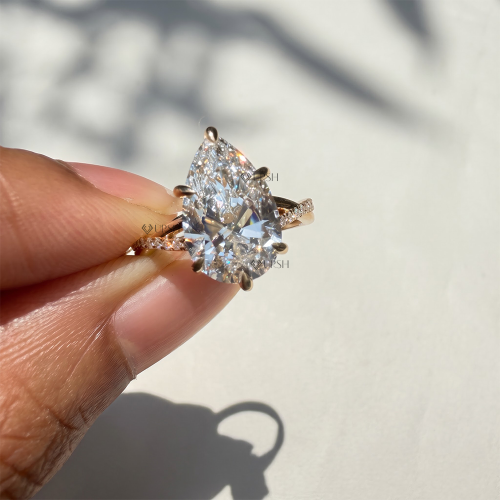 Close-up holding solid gold pear solitaire ring highlighting 6-claw basket and ribbon crossover