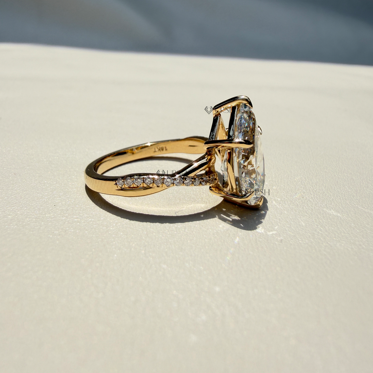 Side profile view of a solid gold pear-cut diamond ring featuring a pave-set band and hidden halo on a neutral surface