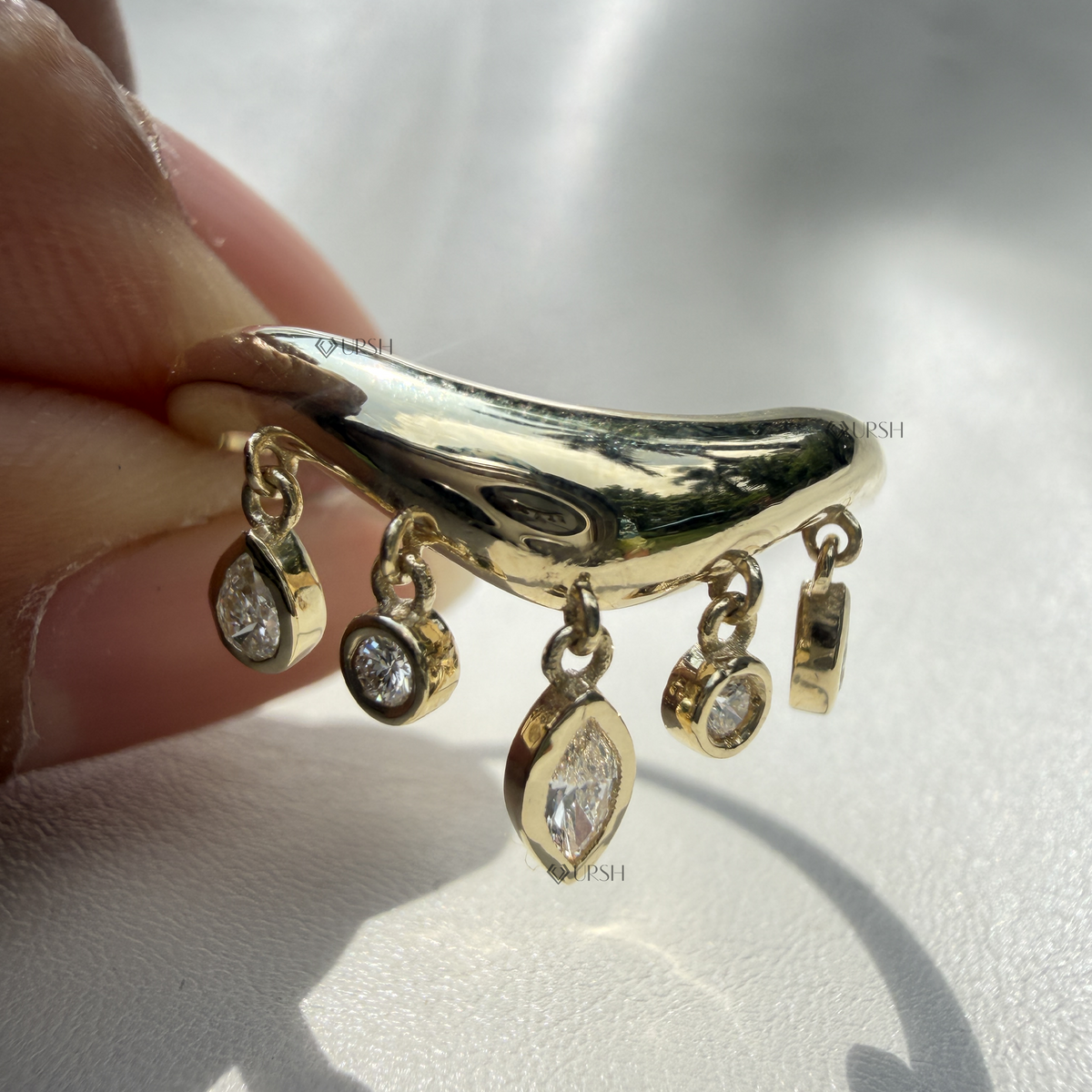 Modern yellow gold curved charm shaker ring worn on finger against neutral background