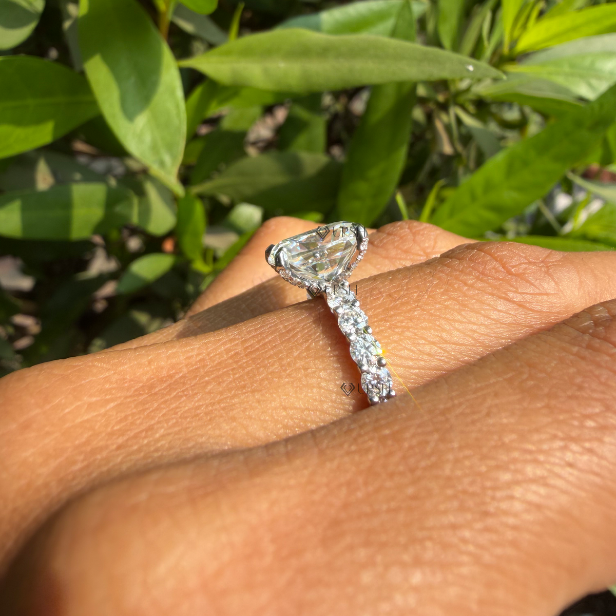Detailed daylight macro close-up holding cushion cut solitaire ring to showcase double-prong corners and facet fire