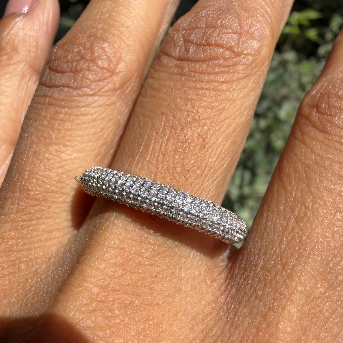 Daylight perspective of domed pavé ring worn against natural background