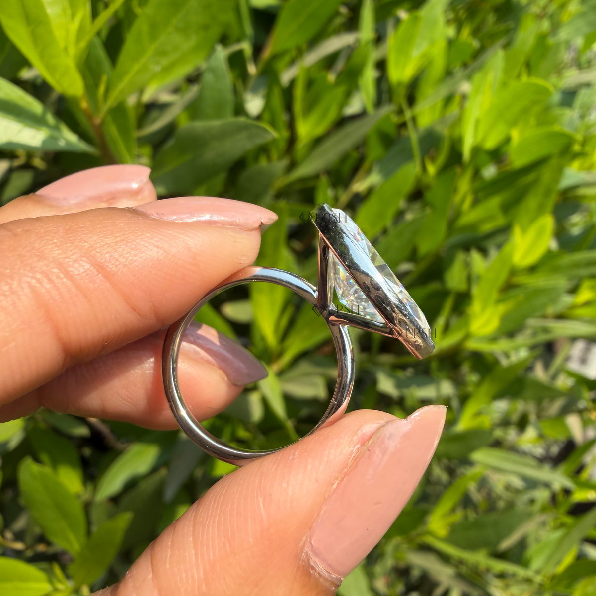 Side profile view of bezel-set east-west marquise ring held against natural outdoor background