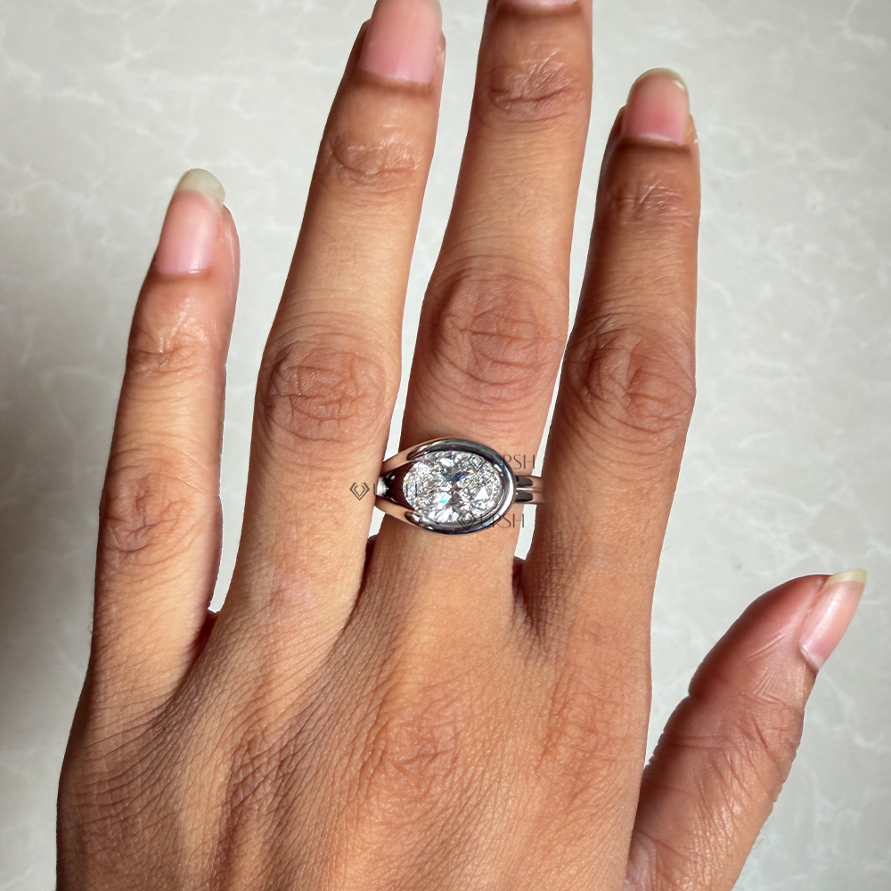 East-west oval diamond modern bypass ring styled across finger in natural lighting