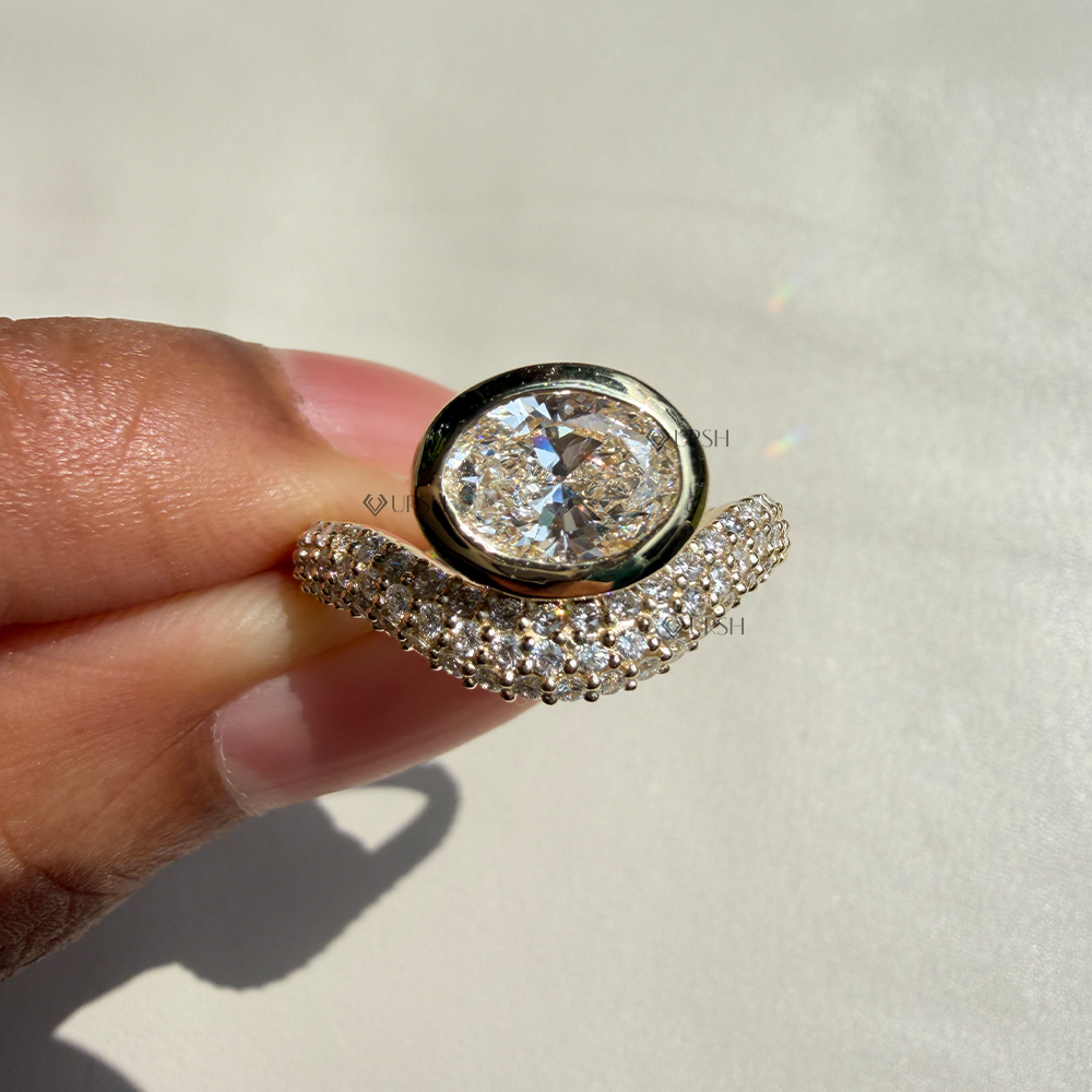Close-up holding solid gold east-west oval ring showcasing thick bezel frame and pave curve