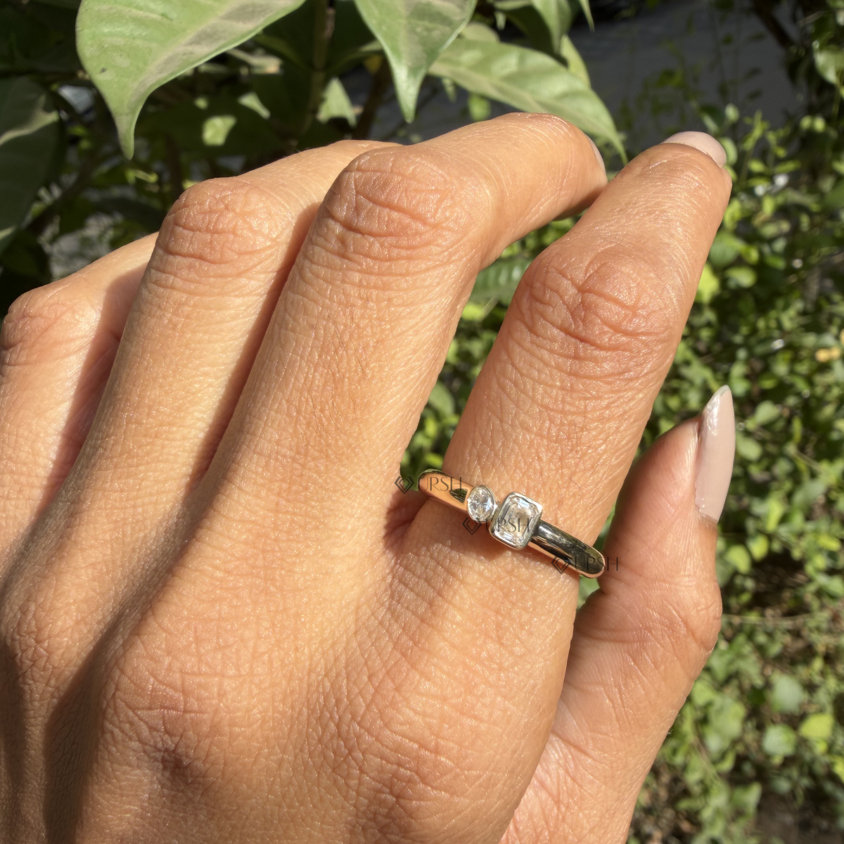 Bezel-set emerald and oval diamond toi et moi ring styled gracefully on finger in natural daylight