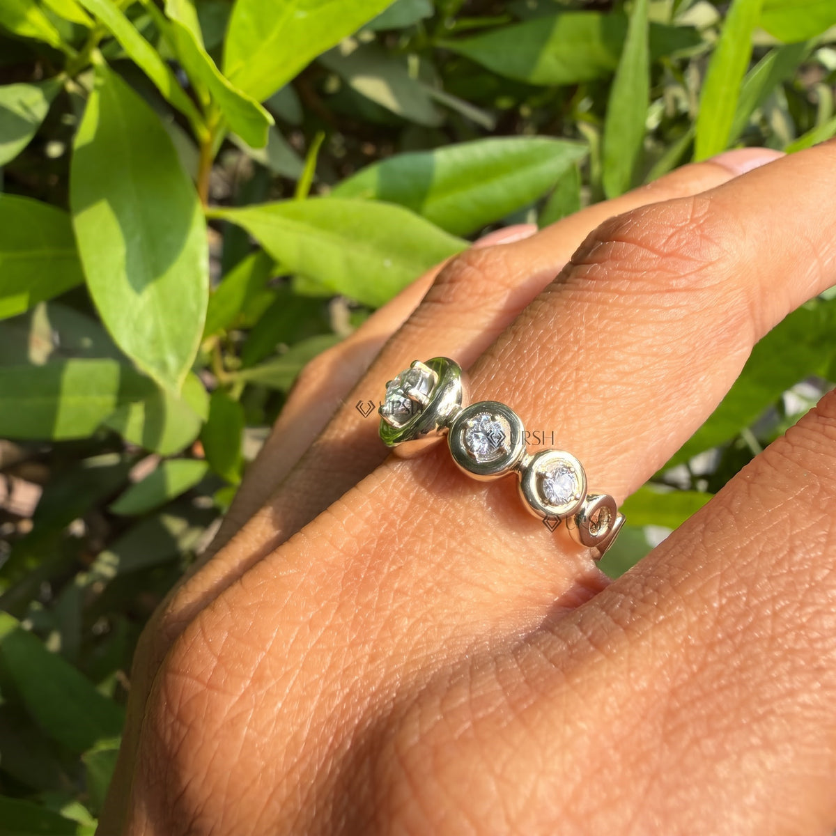 Yellow gold graduated round diamond bezel ring worn against natural garden greenery.