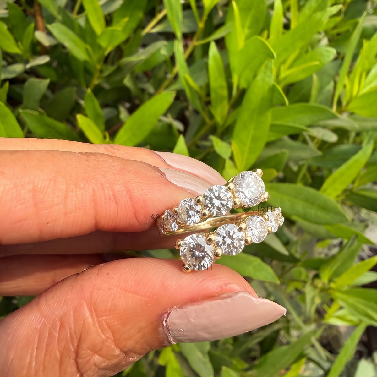 Detailed daylight close-up of graduated round lab diamonds in prong-set bypass rows held against garden foliage