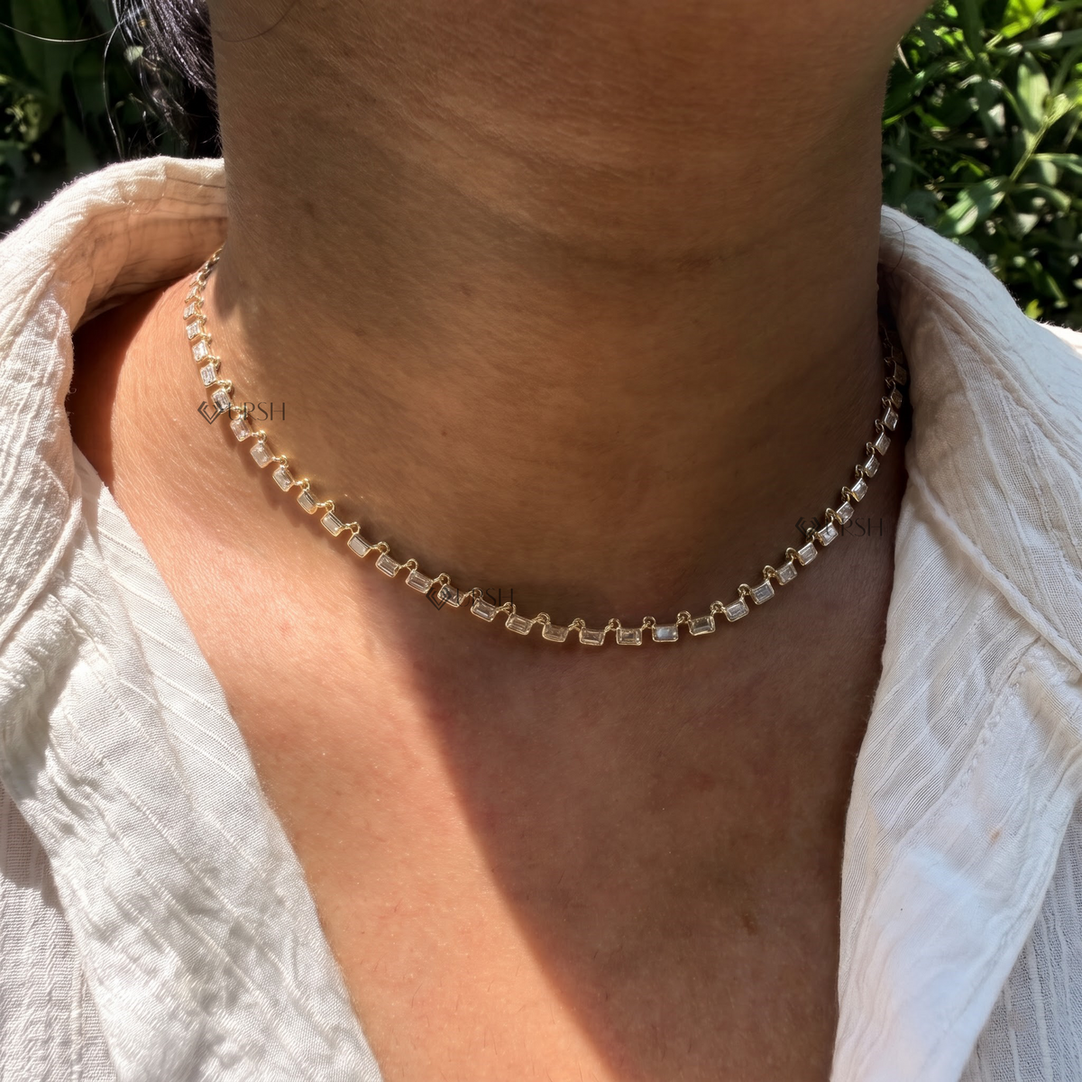 Daylight angle view of yellow gold east-west emerald cut diamond tennis chain worn on neck
