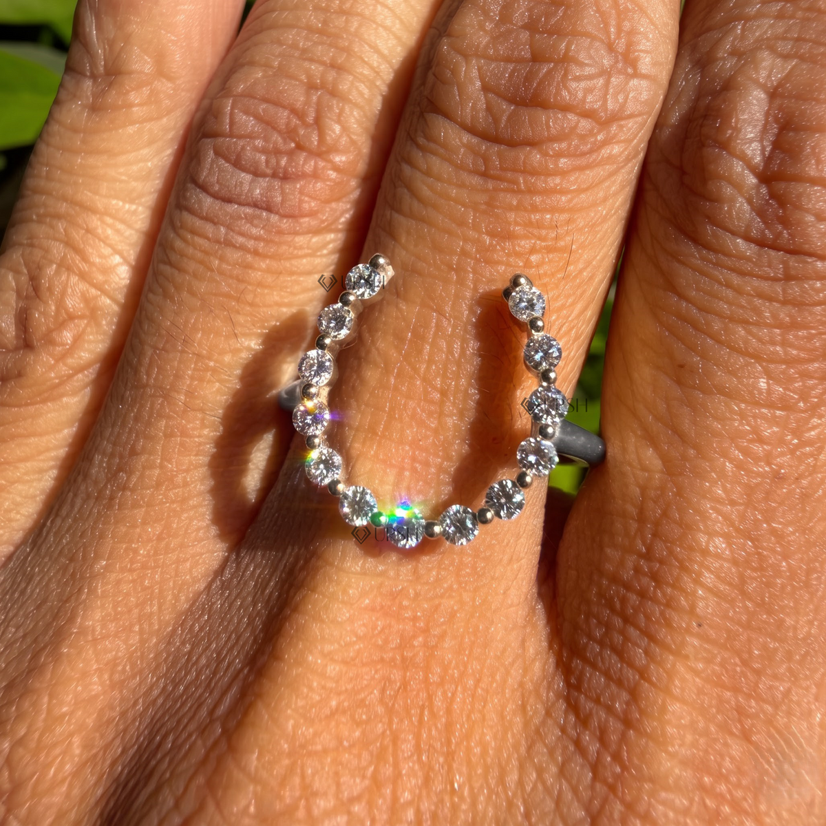 Lucky diamond horseshoe ring catching bright sunlight on ring finger