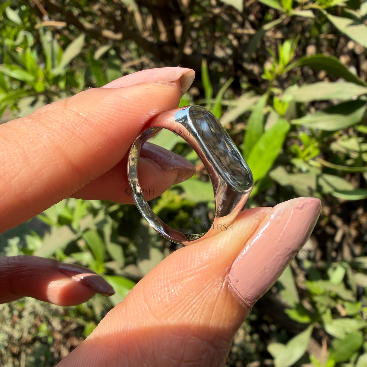 Detailed daylight macro close-up of polished white gold oval signet ring worn on finger