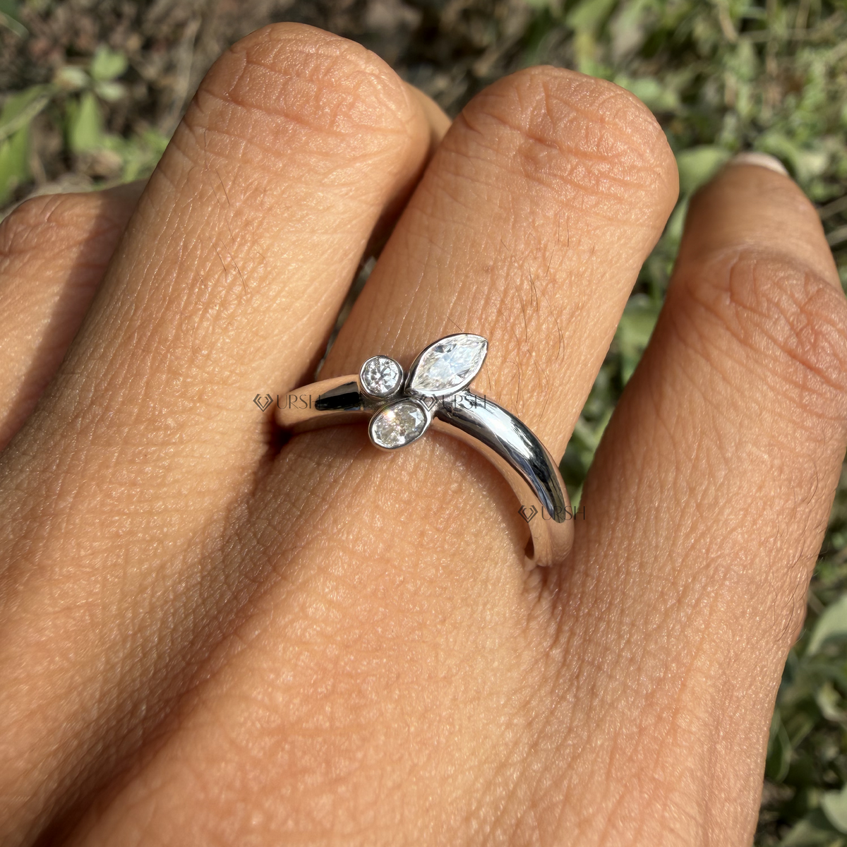 Detailed daylight macro close-up of bezel-set round, marquise, and pear diamond asymmetric cluster on curved band worn on finger