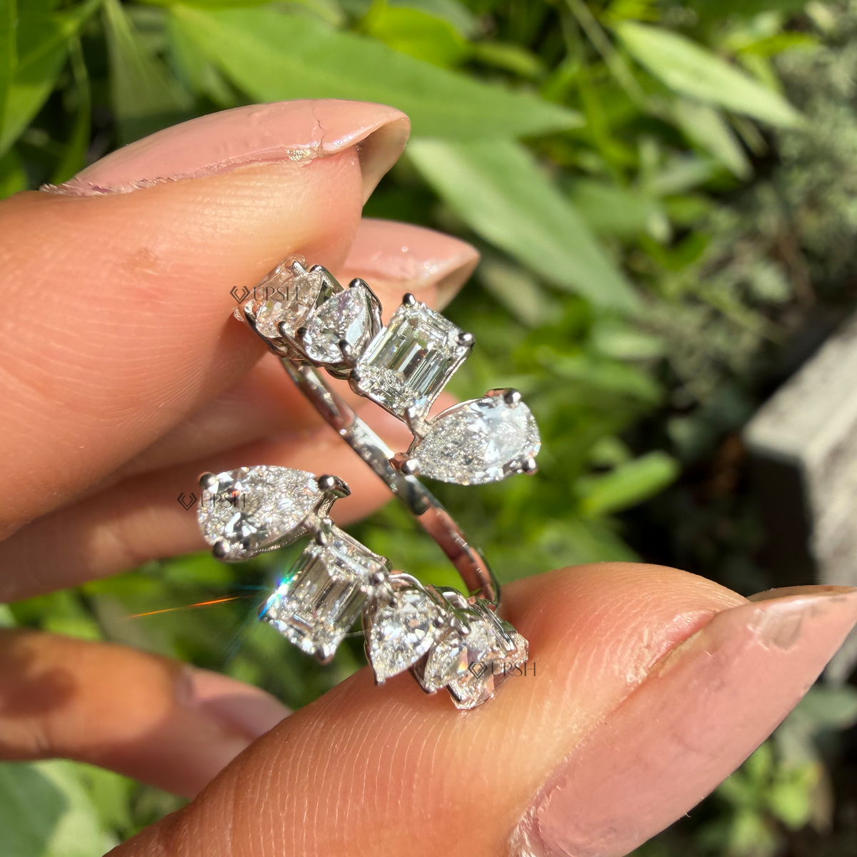 Detailed daylight macro close-up of mixed multi-shape lab diamonds (emerald, pear, round) on bypass wrap band held between fingers