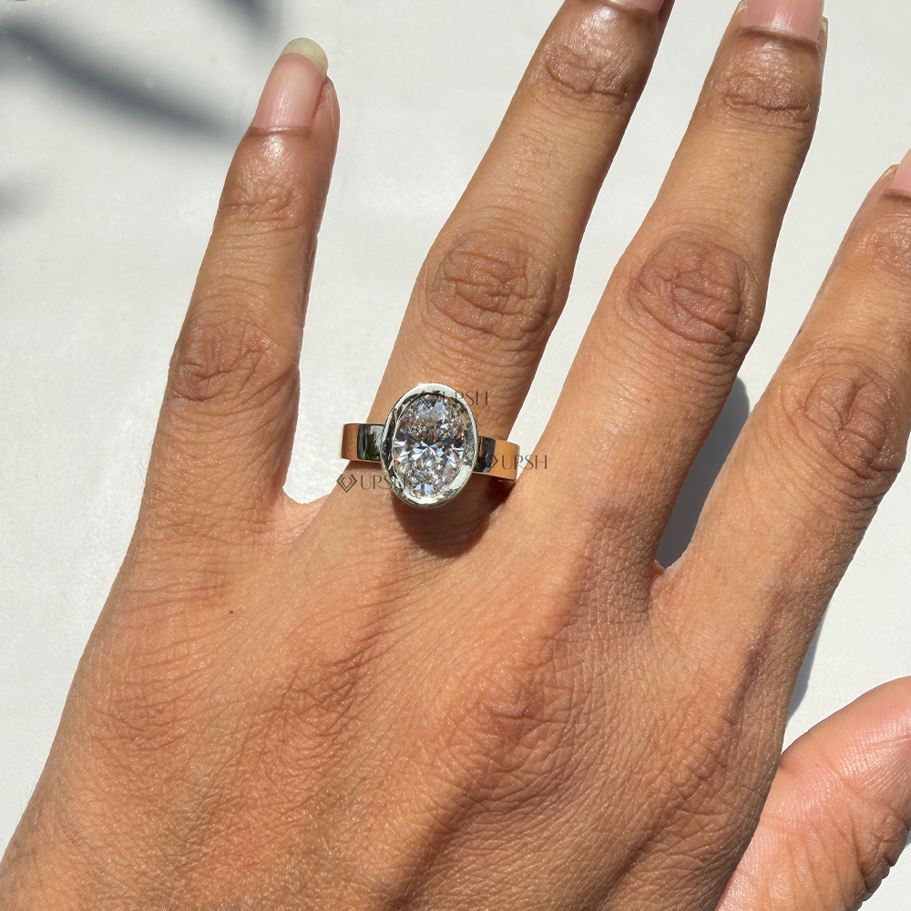 Oval lab diamond bezel ring on wide flat gold band worn on hand outdoors