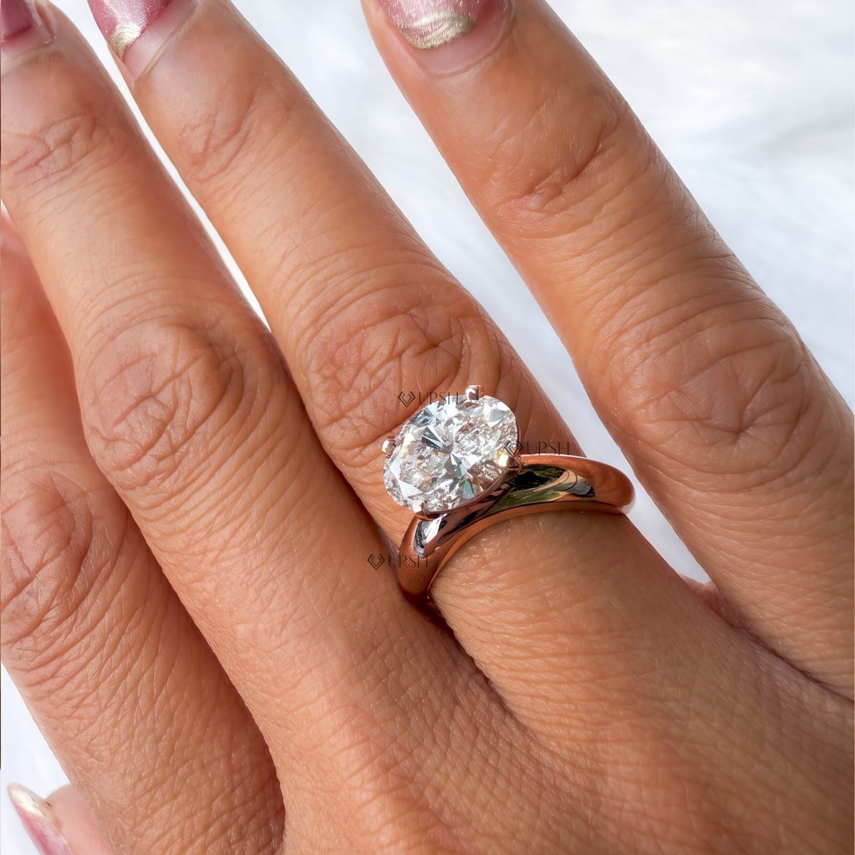 A close-up of a hand wearing a solitaire diamond ring with a rose gold band. The ring features a round brilliant-cut diamond set in a rose gold prong setting, shown on a finger against a soft white background.