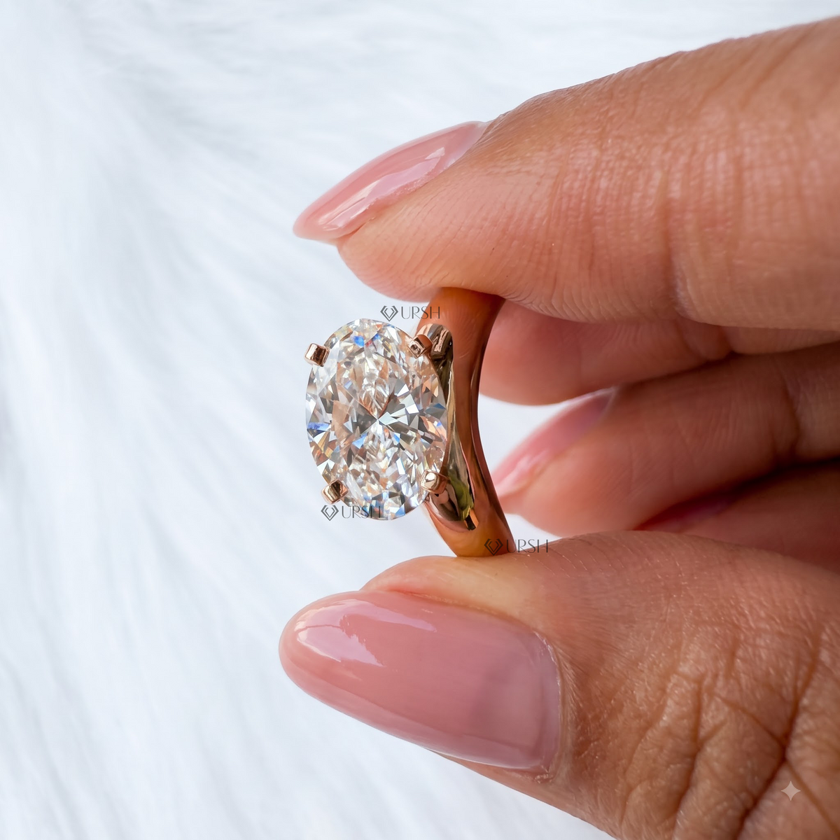 A close-up of a hand holding a rose gold ring with a large oval-cut clear gemstone, set against a soft white textured background.