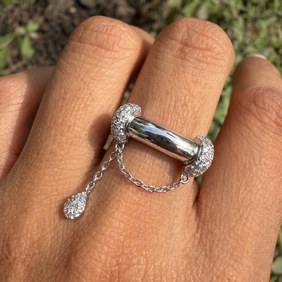 Close-up daylight angle view of white gold statement ring worn on finger displaying hanging pear charm and chain link