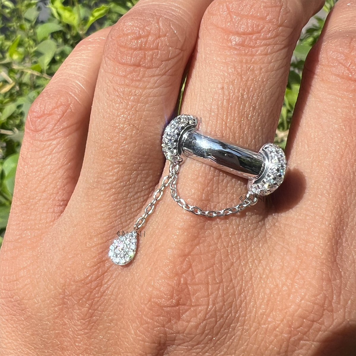 Detailed daylight macro close-up of pavé diamond collars, connecting chain, and dangling pear charm worn on finger