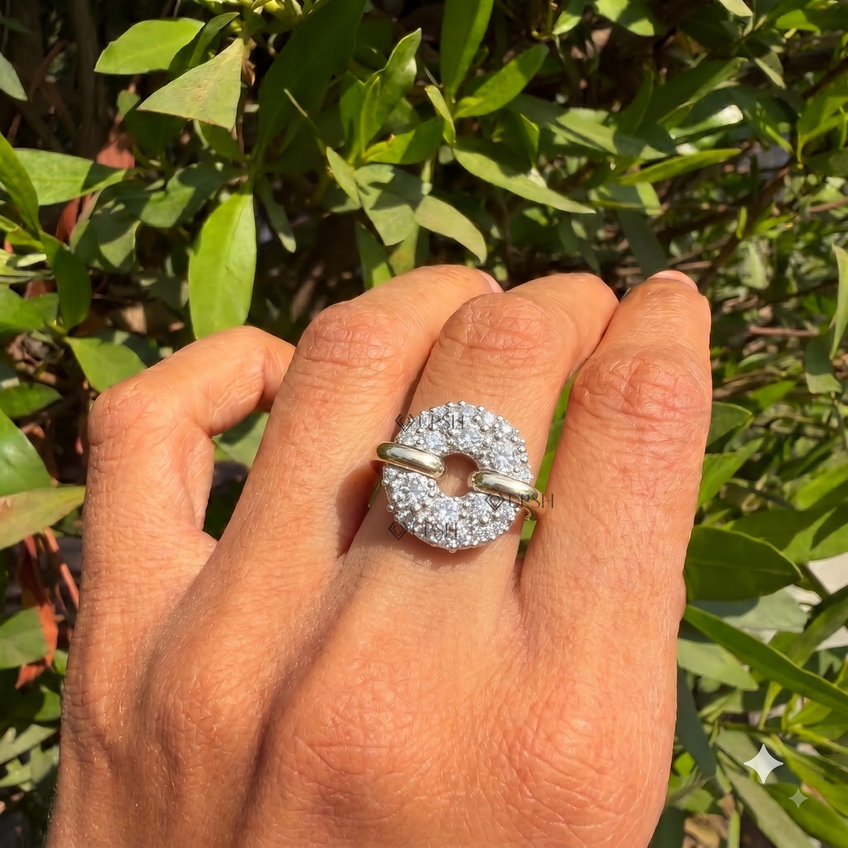 Top-down view of a circular pavé-set diamond statement ring worn on a hand against a green foliage background.