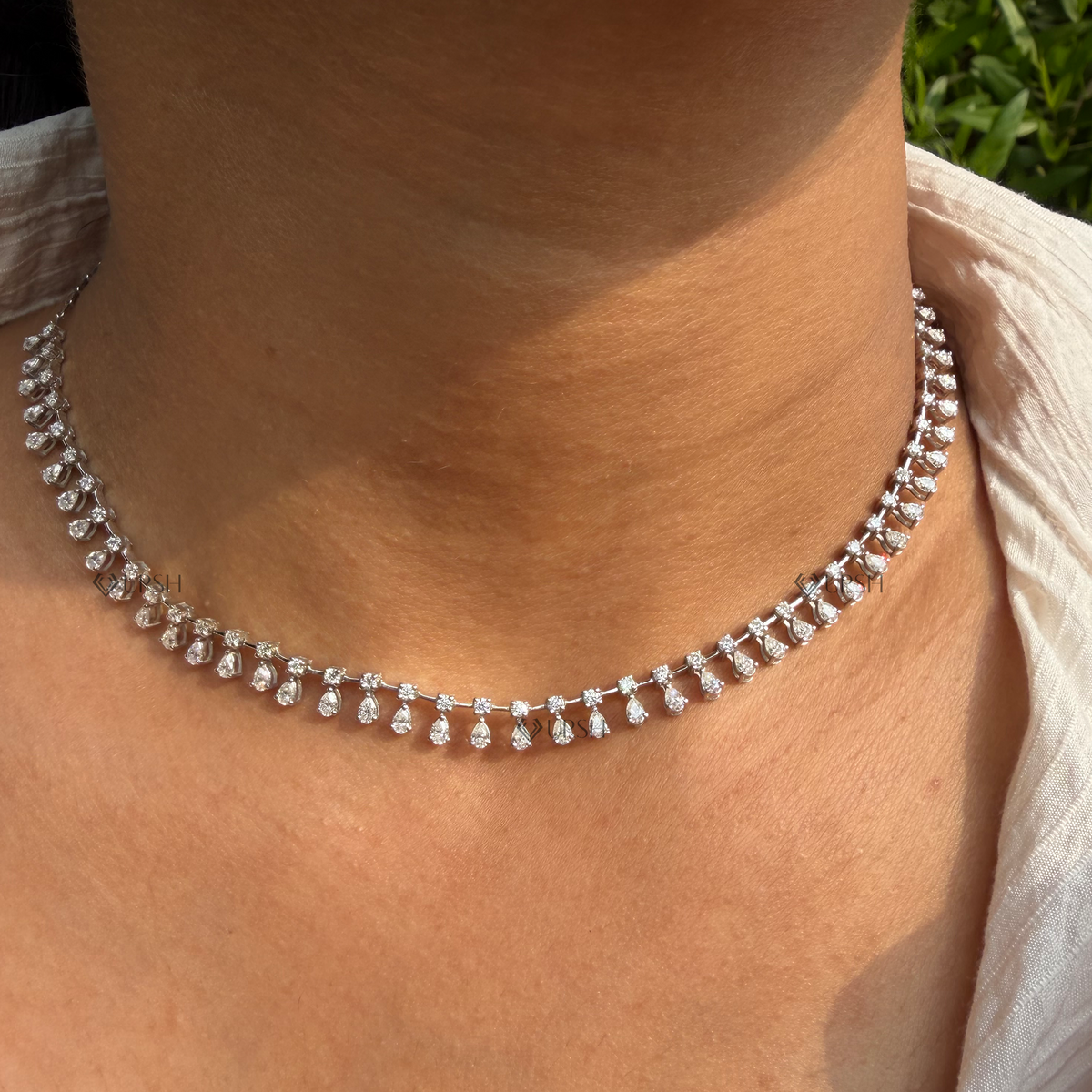 Daylight perspective view of white gold pear and round diamond dangle fringe chain worn on neck