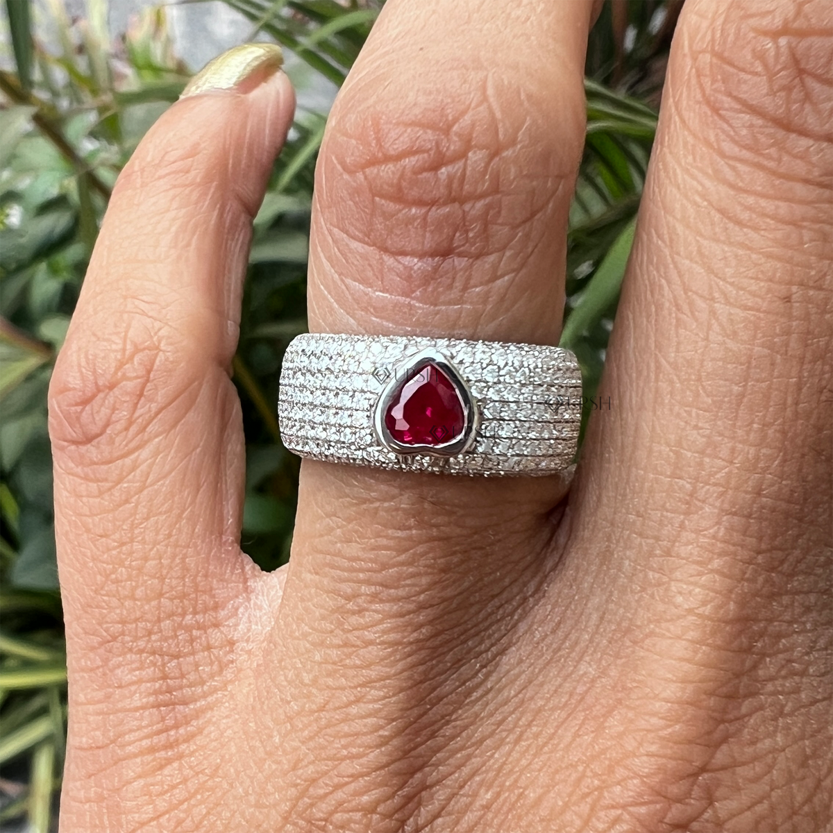 Daylight perspective of white gold pavé diamond and ruby ring worn against natural background