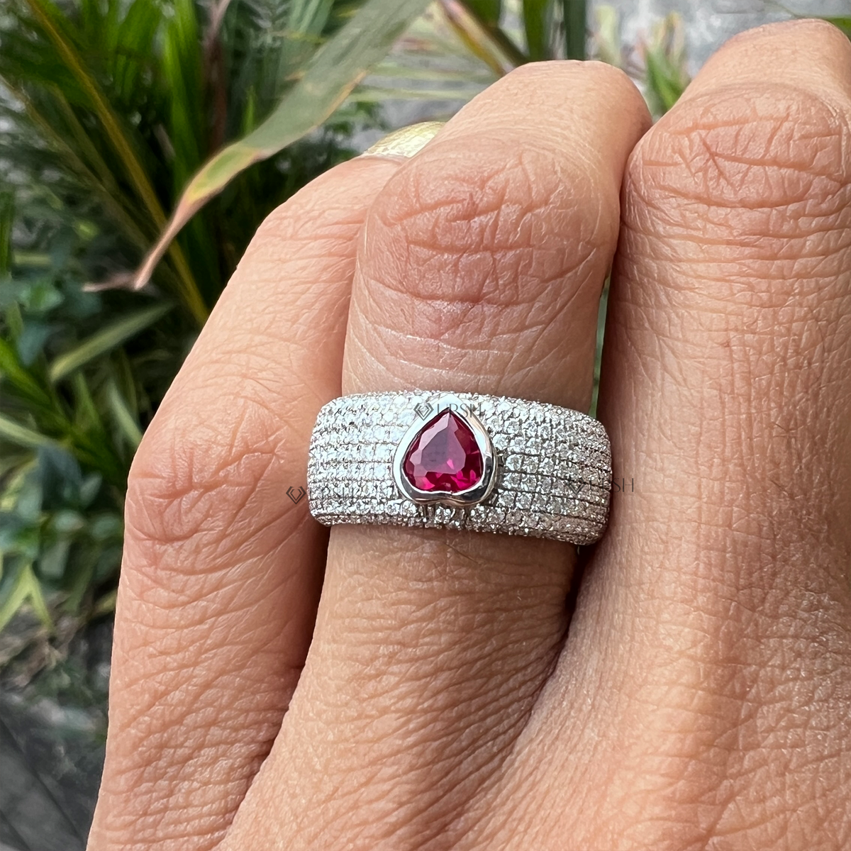 Detailed daylight macro close-up of bezel-set heart ruby center surrounded by multi-row micro-pavé diamonds worn on finger