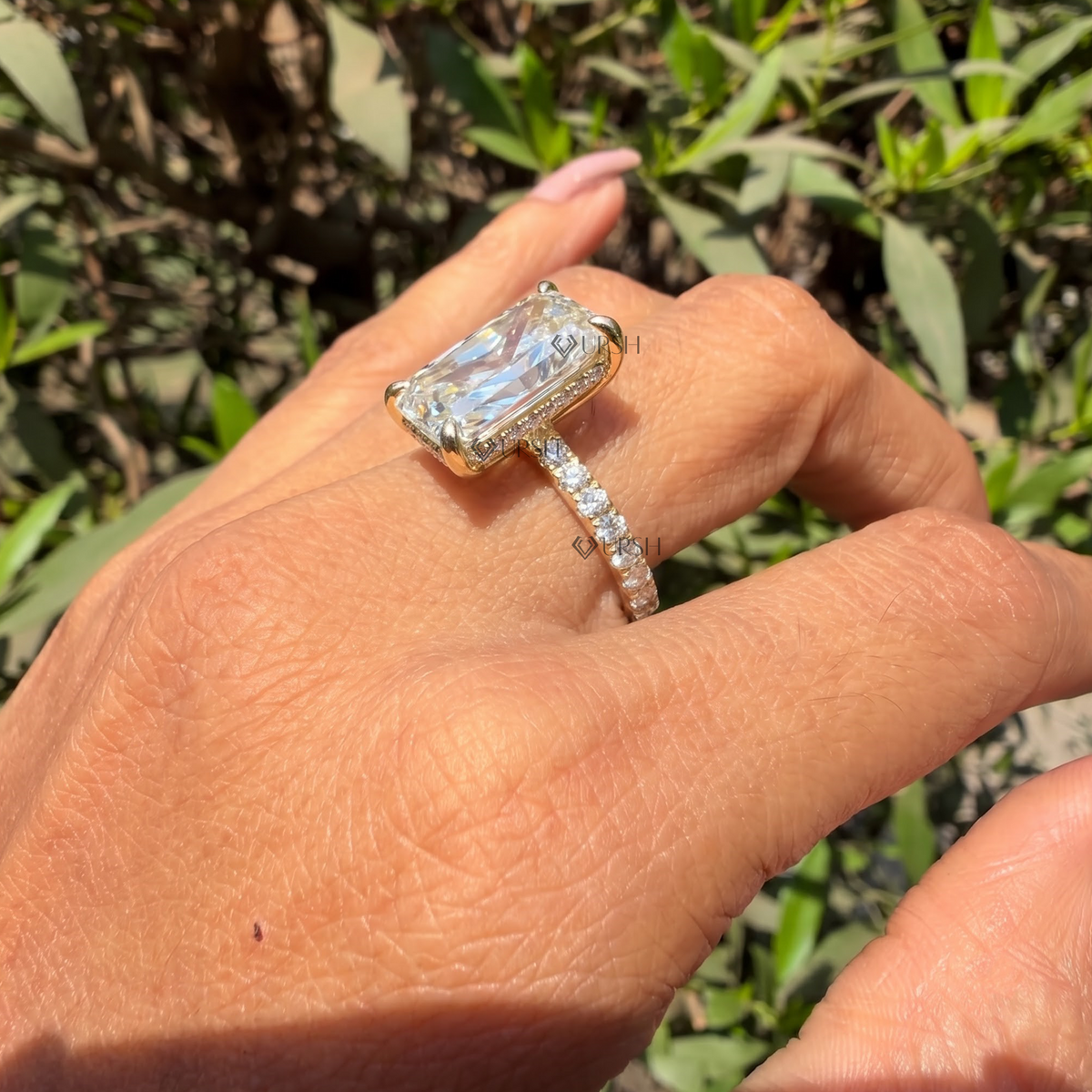 Detailed daylight close-up of radiant cut lab diamond and pavé band worn on hand against foliage