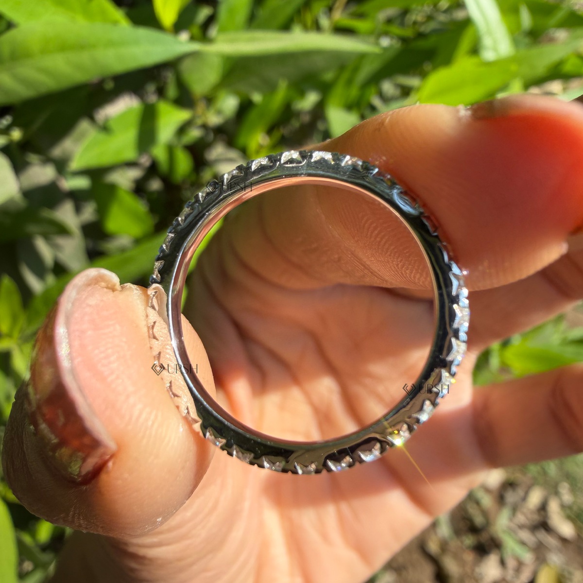 Detailed daylight macro close-up of full eternity diamond band worn on finger showing shared-prong fire