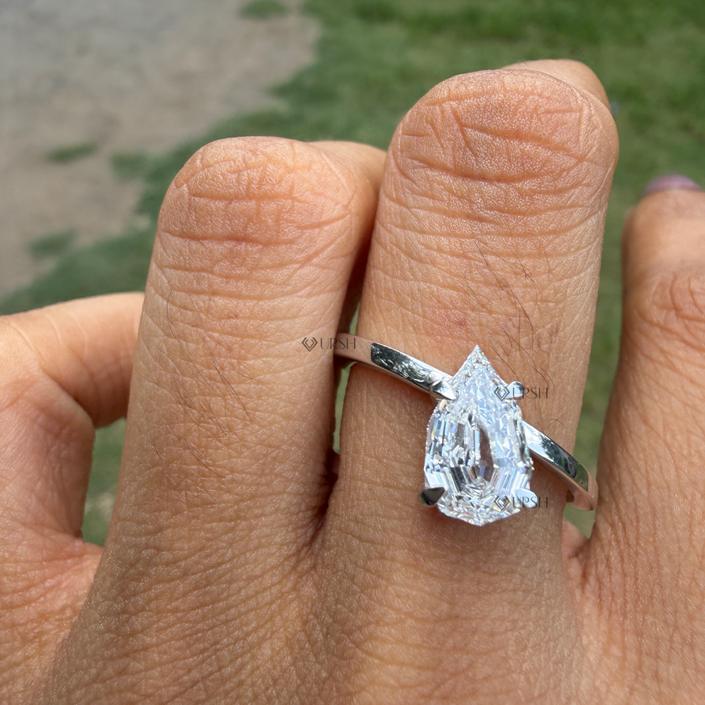 Step cut pear diamond bypass engagement ring worn on finger in natural daylight