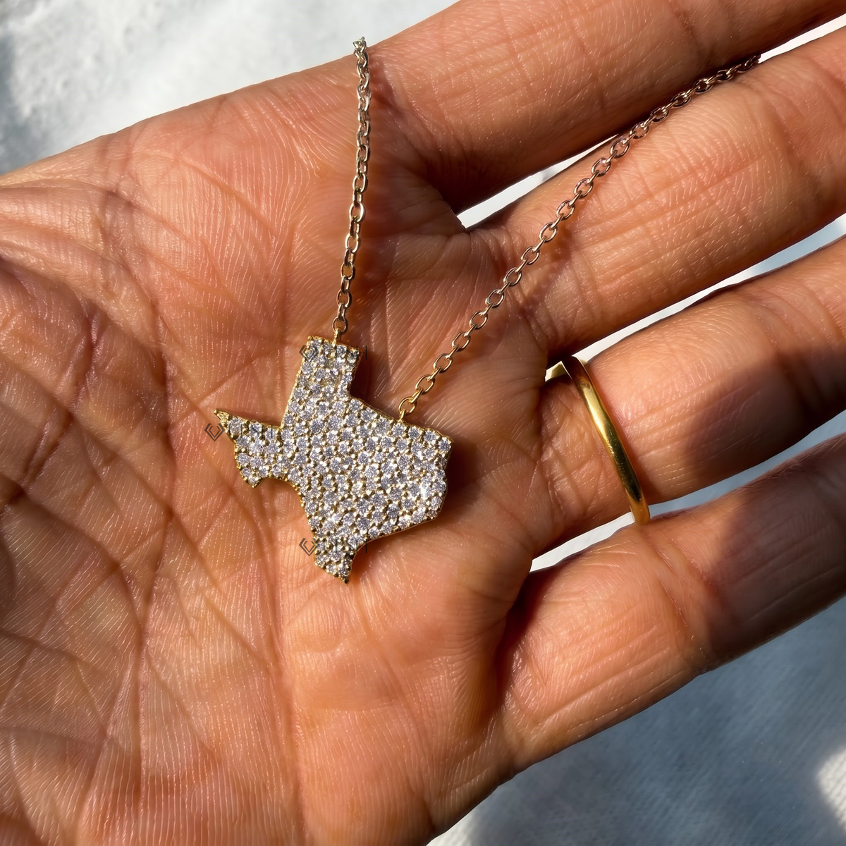 Detailed hand model view of solid yellow gold Texas state map pavé diamond pendant held gracefully