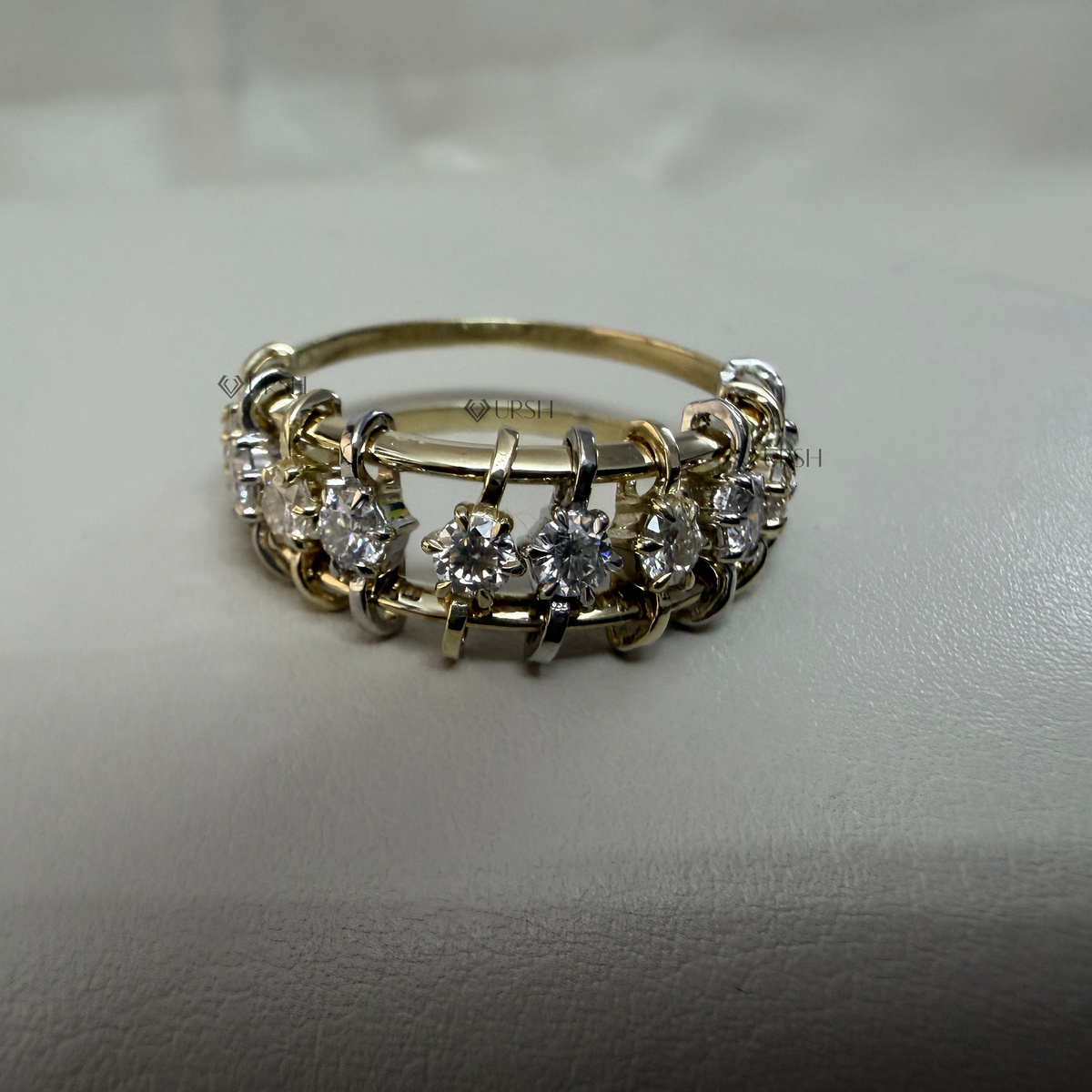 Studio view of a two-tone gold multi-row diamond band ring on a neutral surface.
