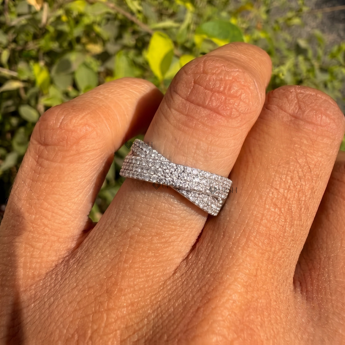 Wide X-shaped crossing pavé statement ring styled gracefully on finger in natural daylight