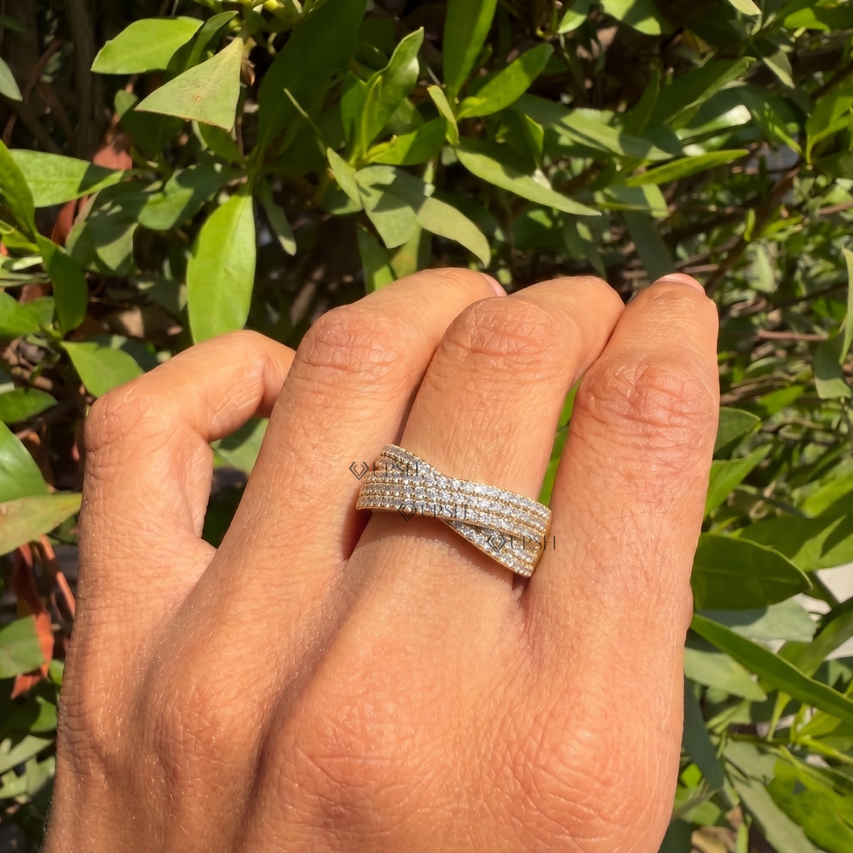 Yellow gold wide criss-cross diamond ring worn against natural garden greenery