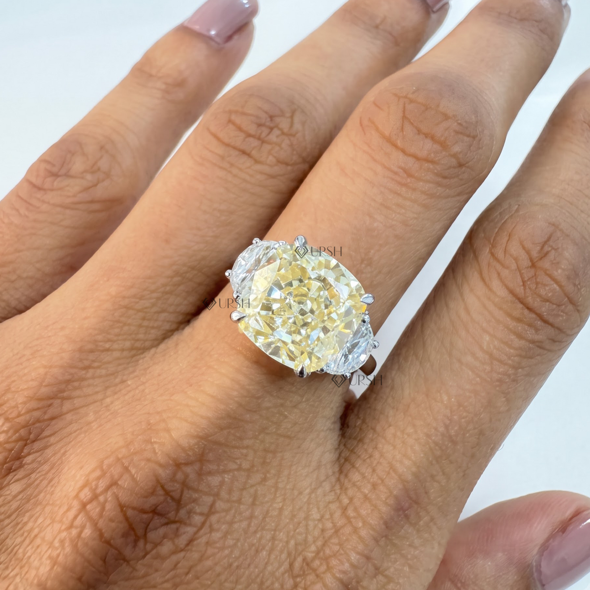 Finger close-up of large vivid yellow cushion diamond trilogy ring held against skin tone