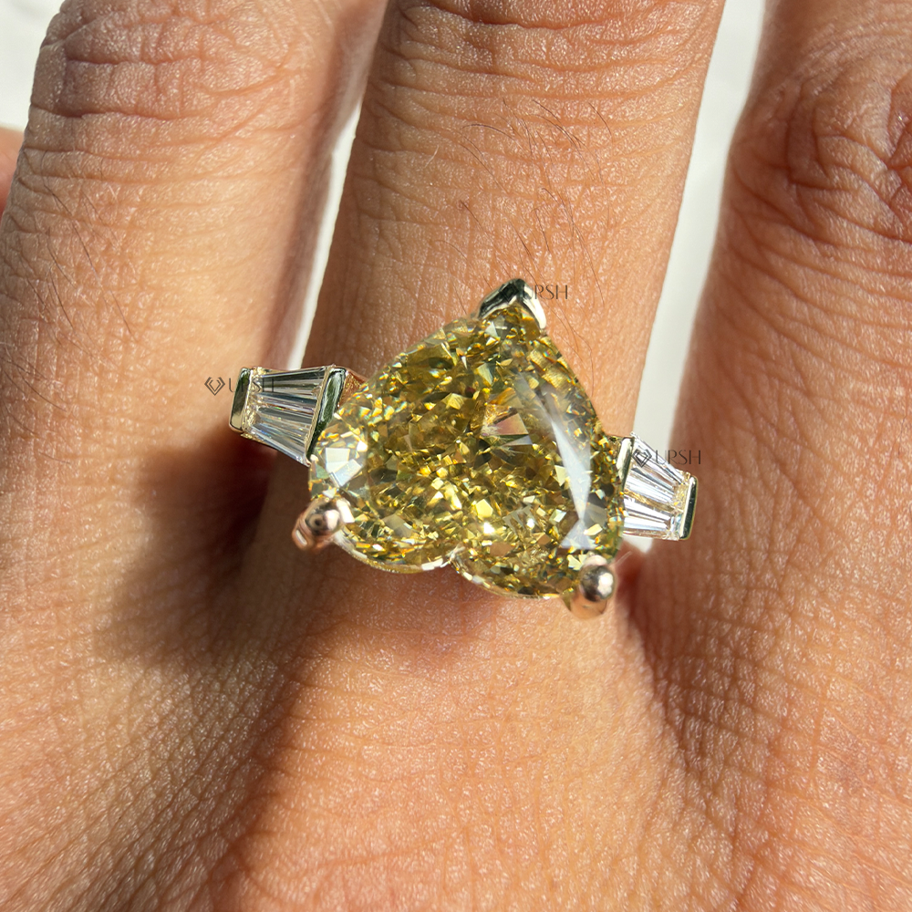 Fancy yellow heart cut diamond three stone engagement ring worn on hand in bright natural daylight