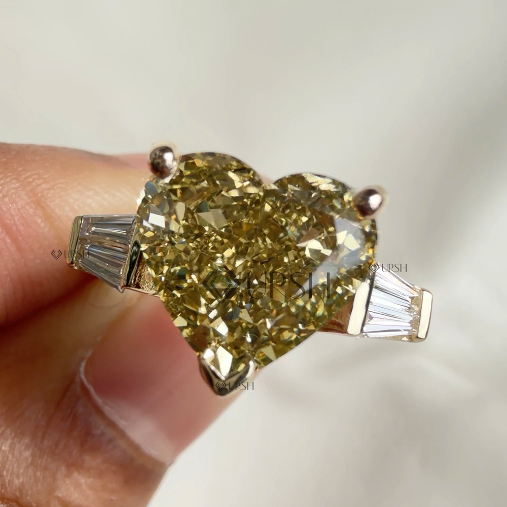 Close-up holding yellow heart diamond ring showing brilliance, V-tip prong, and step cut baguettes