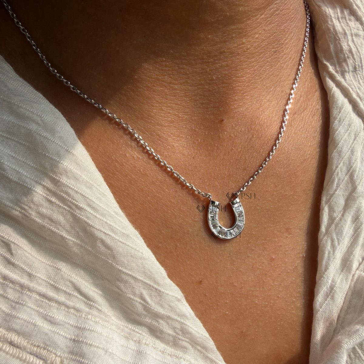 Daylight perspective view of white gold baguette diamond horseshoe pendant chain worn on neck