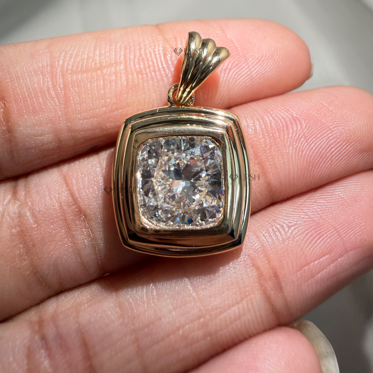 Detailed hand model view of solid yellow gold tiered cushion bezel pendant held between fingers