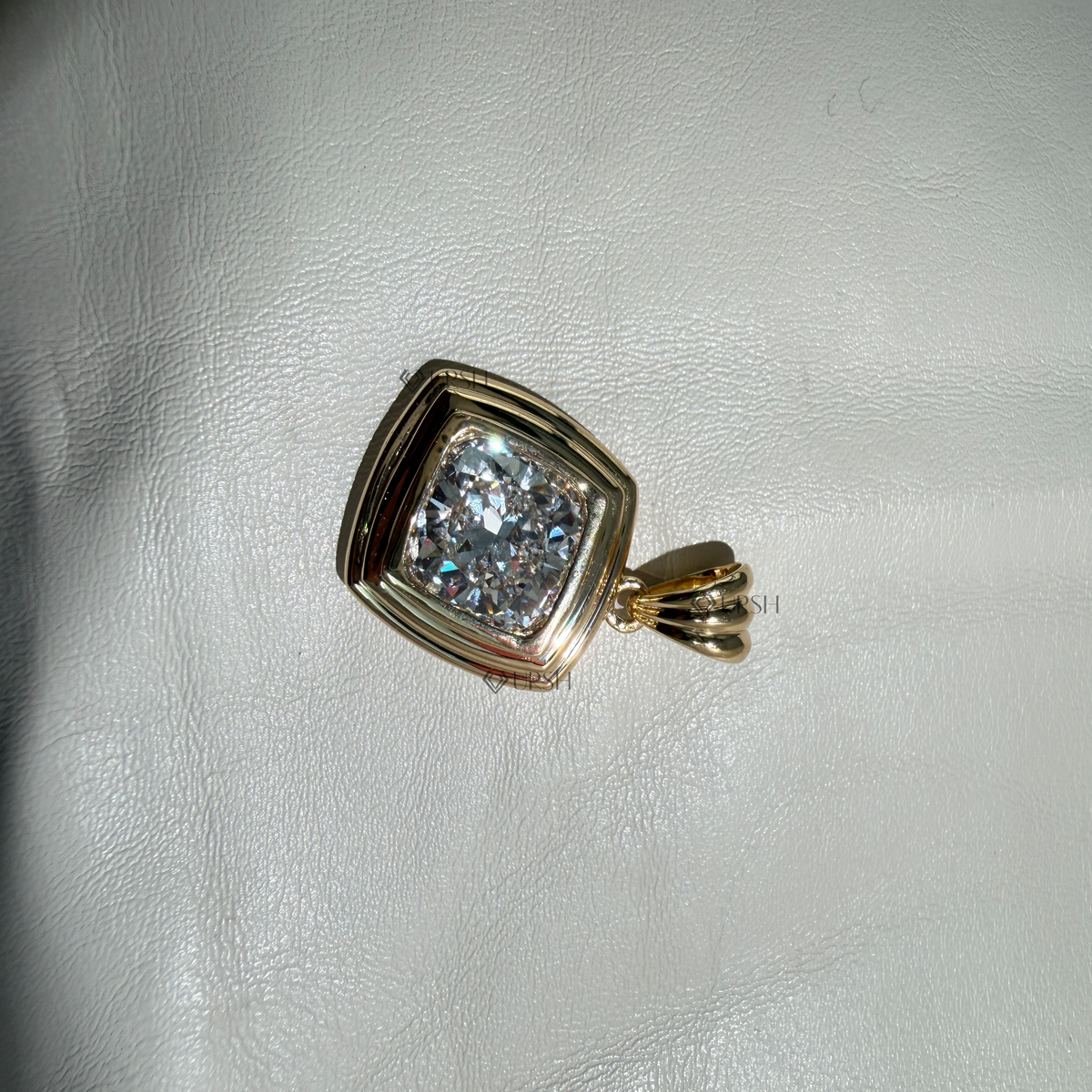 Solid yellow gold tiered cushion bezel pendant resting flat on neutral surface