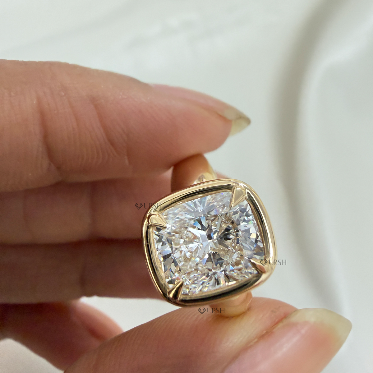 Close-up holding yellow gold cushion cut diamond ring showcasing rounded puffy bezel rim
