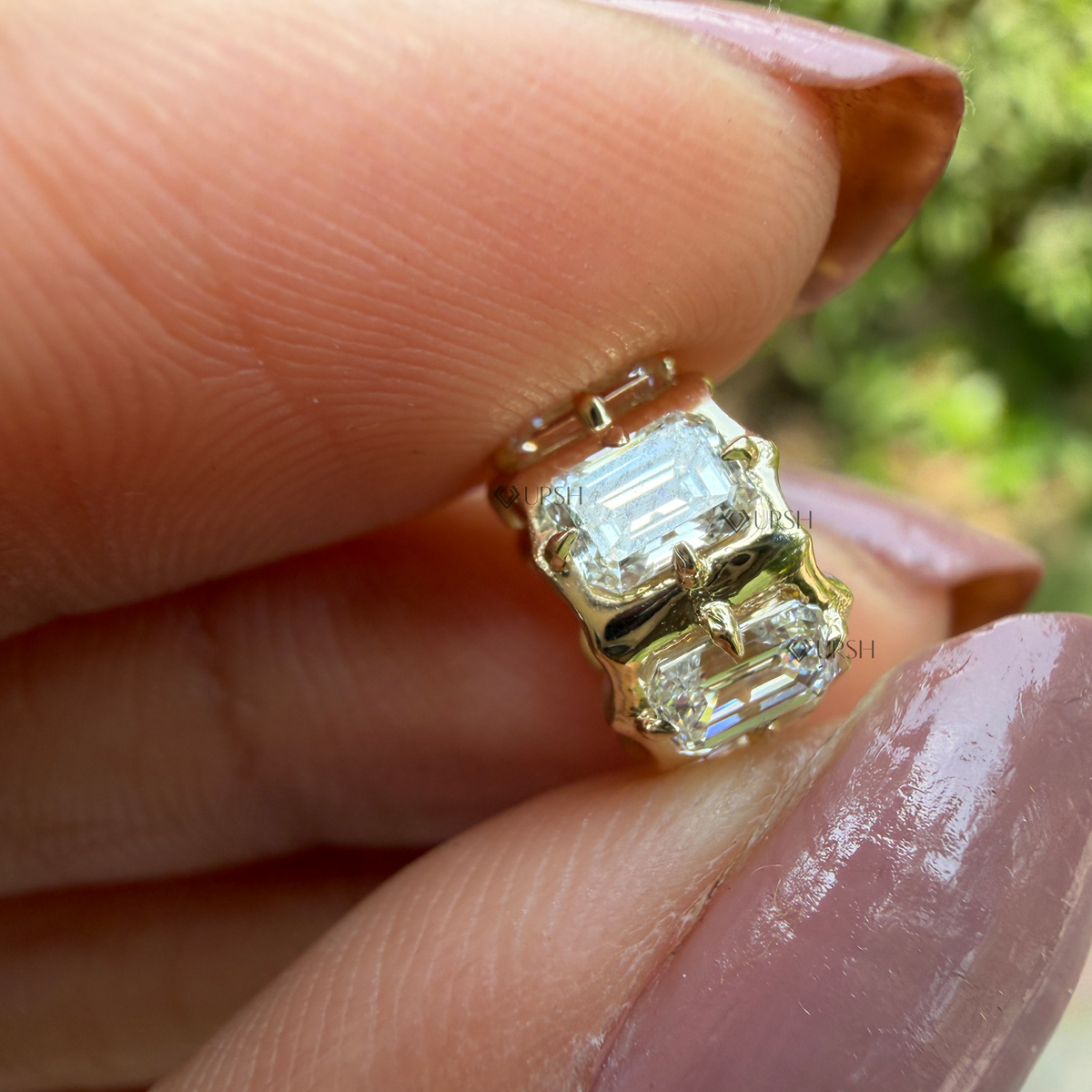 Detailed macro view of solid yellow gold hexagonal barrel bead charm set with emerald cut diamonds held between fingers